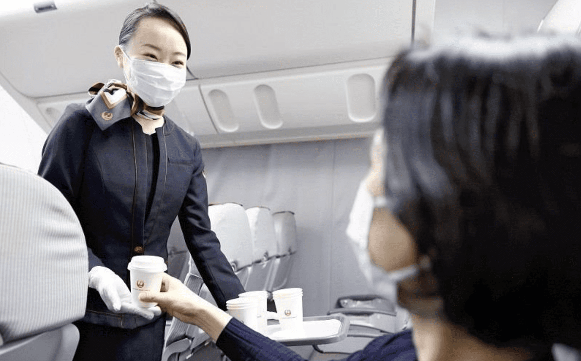 Tiếp viên hàng không JAL thu hồi cốc nhựa từ hành khách - Ảnh: Yomiuri Shimbun